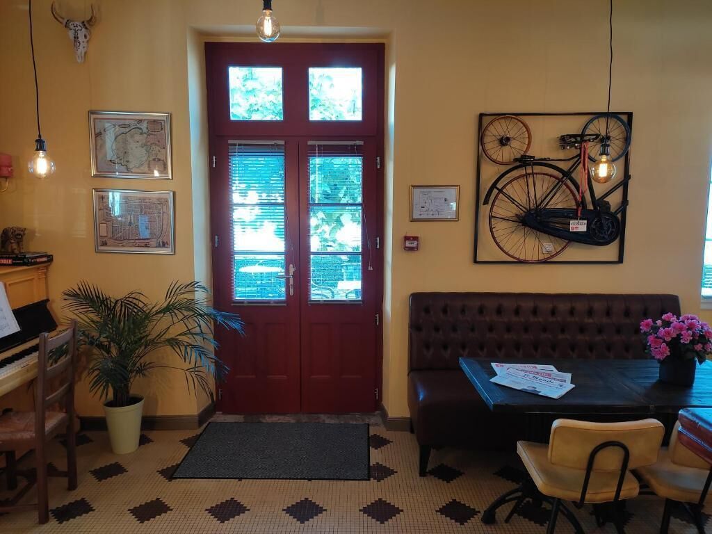 A reception area with a piano, a potted plant, a brown sofa, a table with papers, and a bicycle artwork on the wall.