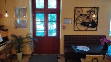 A reception area with a piano, a potted plant, a brown sofa, a table with papers, and a bicycle artwork on the wall.