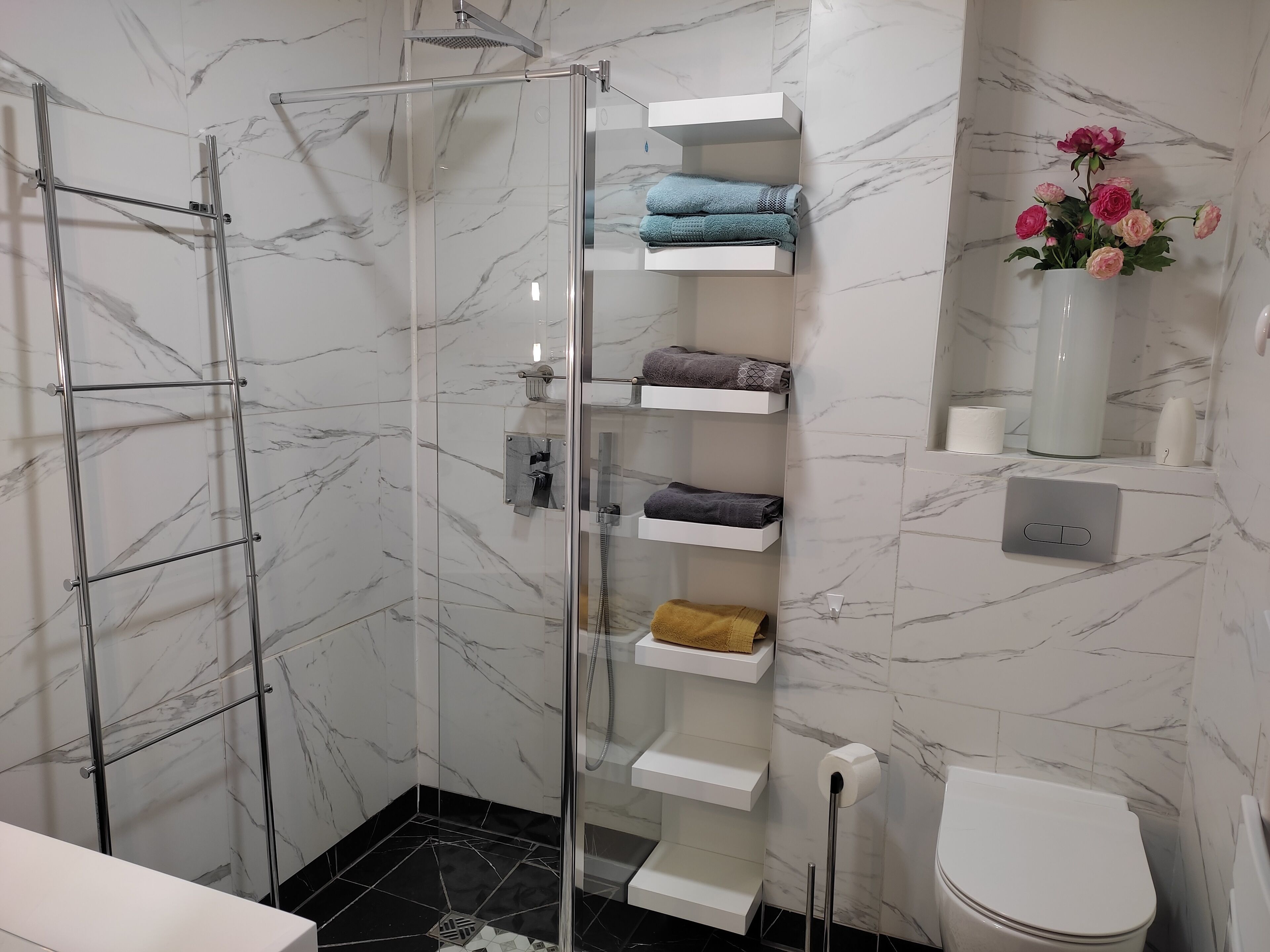 Uma casa de banho moderna com chuveiro em cabine de vidro, paredes de mármore e sanita.