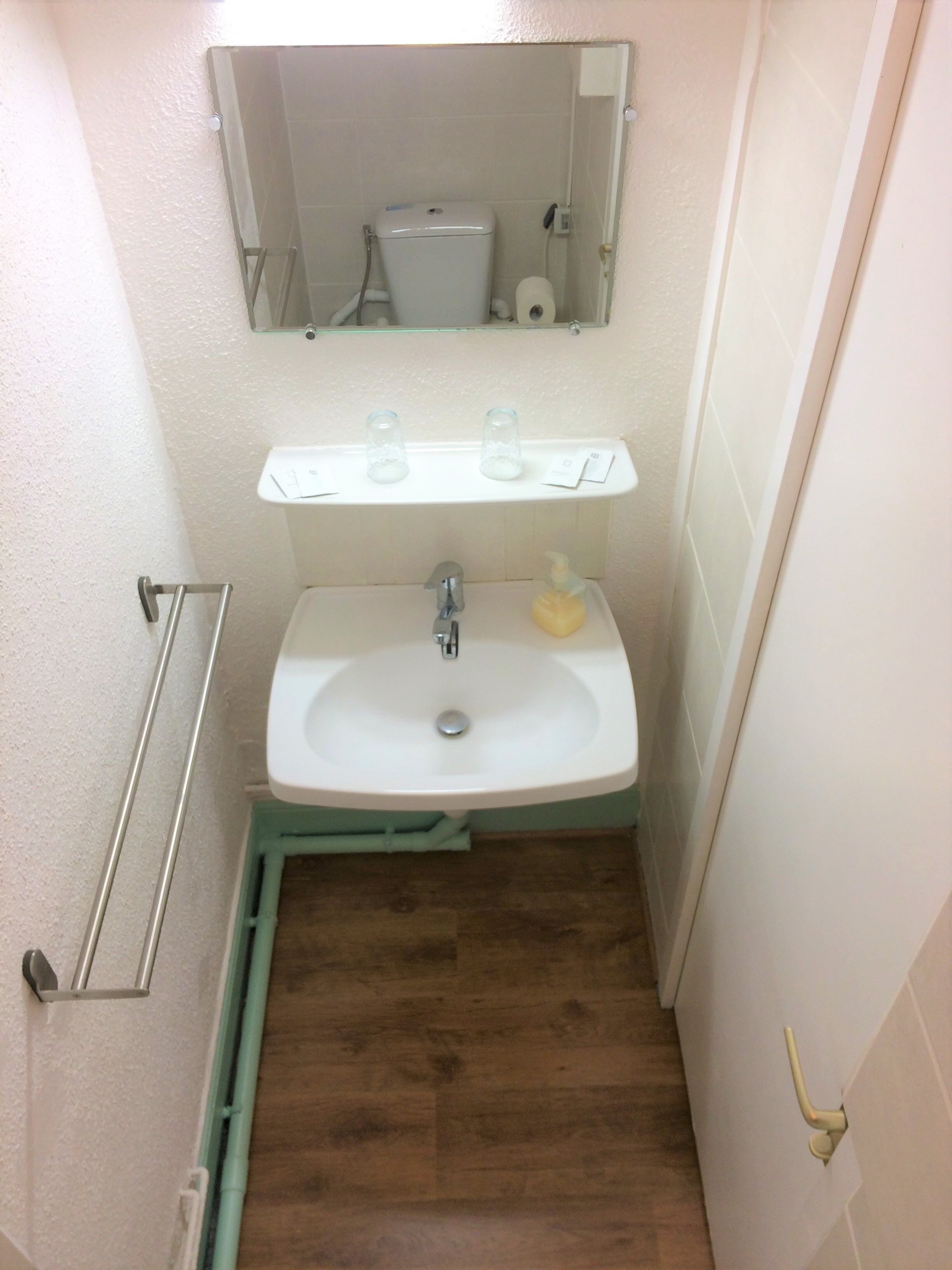 A small bathroom with a white sink, a mirror above it, and a toilet visible in the background.