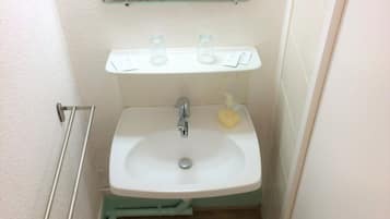 Een kleine badkamer met een witte wastafel, een spiegel erboven en een toilet in de achtergrond.