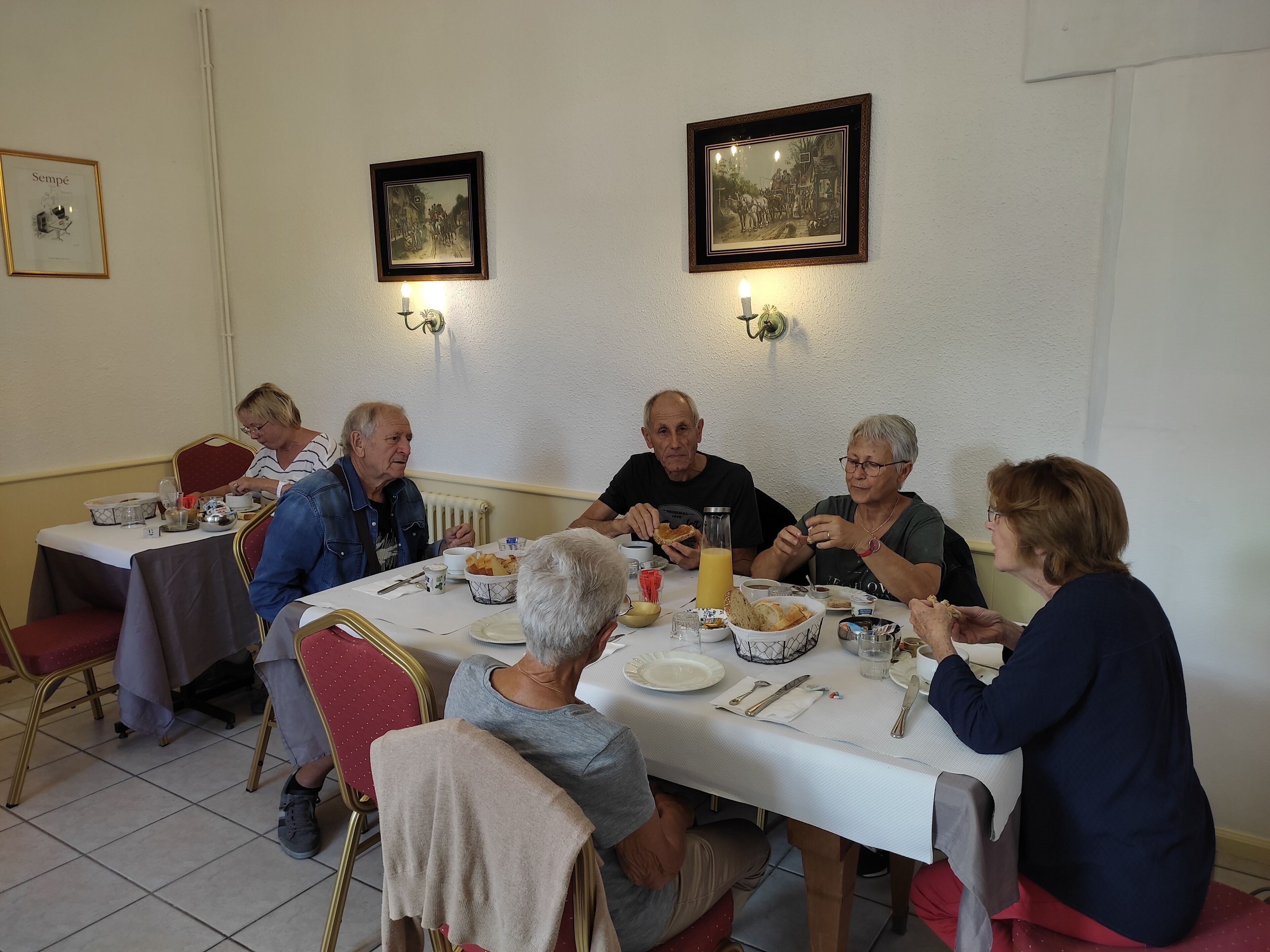 Un groupe de personnes est assis à une table recouverte d’une nappe blanche, entourée de chaises dotées de coussins rouges.