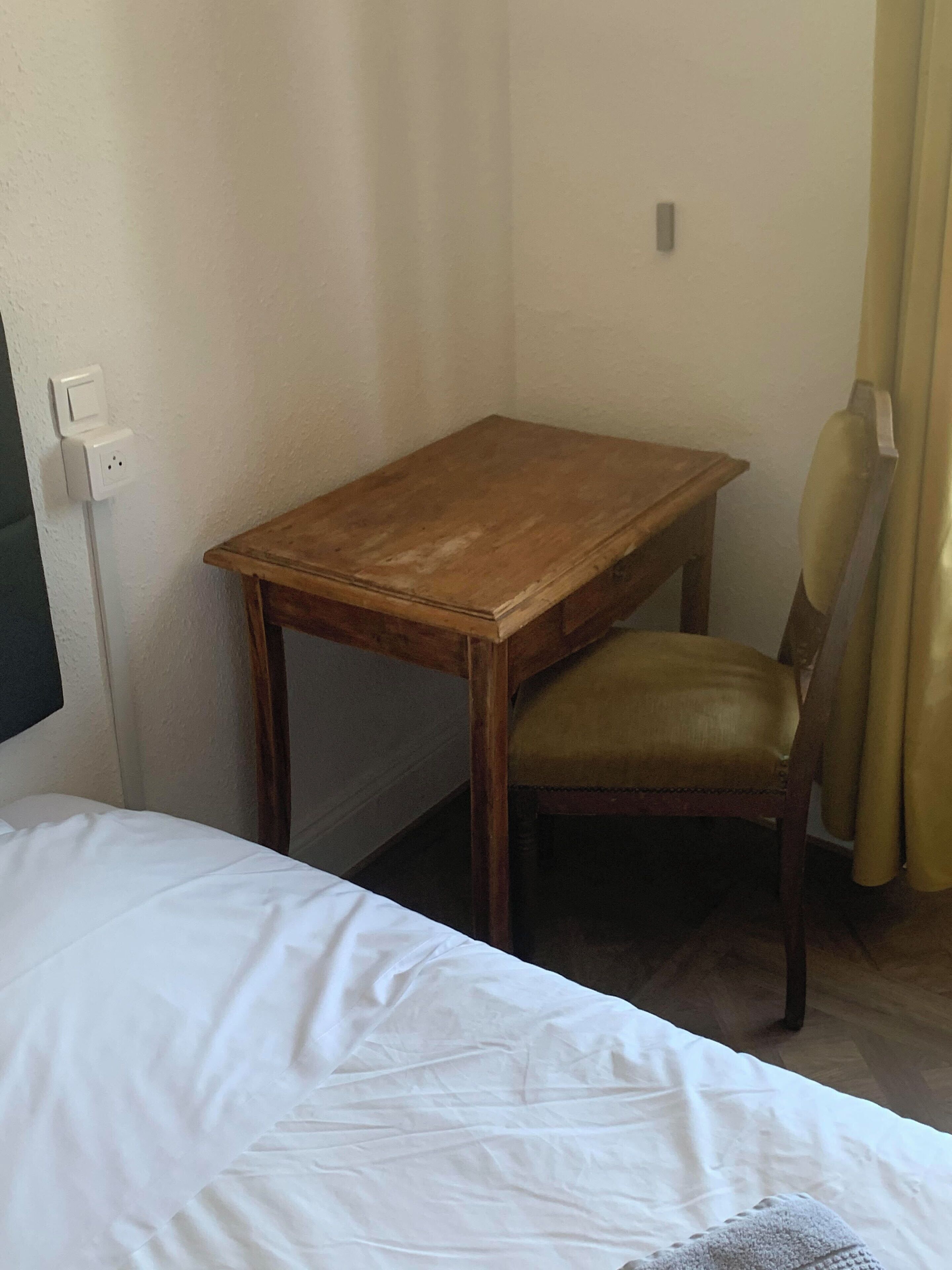 Et hotelværelse med et træskrivebord, en læderstol og en seng med hvide sengetøj.