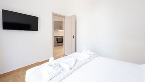A hotel room with a bed, a flat-screen TV mounted on the wall, and a wooden floor. - Modern 2-bedroom Gem Close to Metro (Athens)