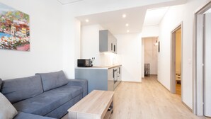 A modern apartment with a grey sofa, a wooden coffee table, and a kitchen area with cabinets and a microwave. - Modern 2-bedroom Gem Close to Metro (Athens)