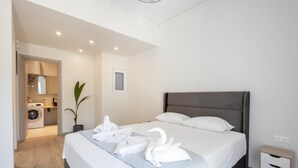 Ett modernt hotellrum med en snyggt bäddad säng, ett litet sängbord och ett tydligt avgränsat område för tvätt.
