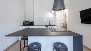 Ett modernt kök med en central köksö, barstolar, en mikrovågsugn och en hängande taklampa.