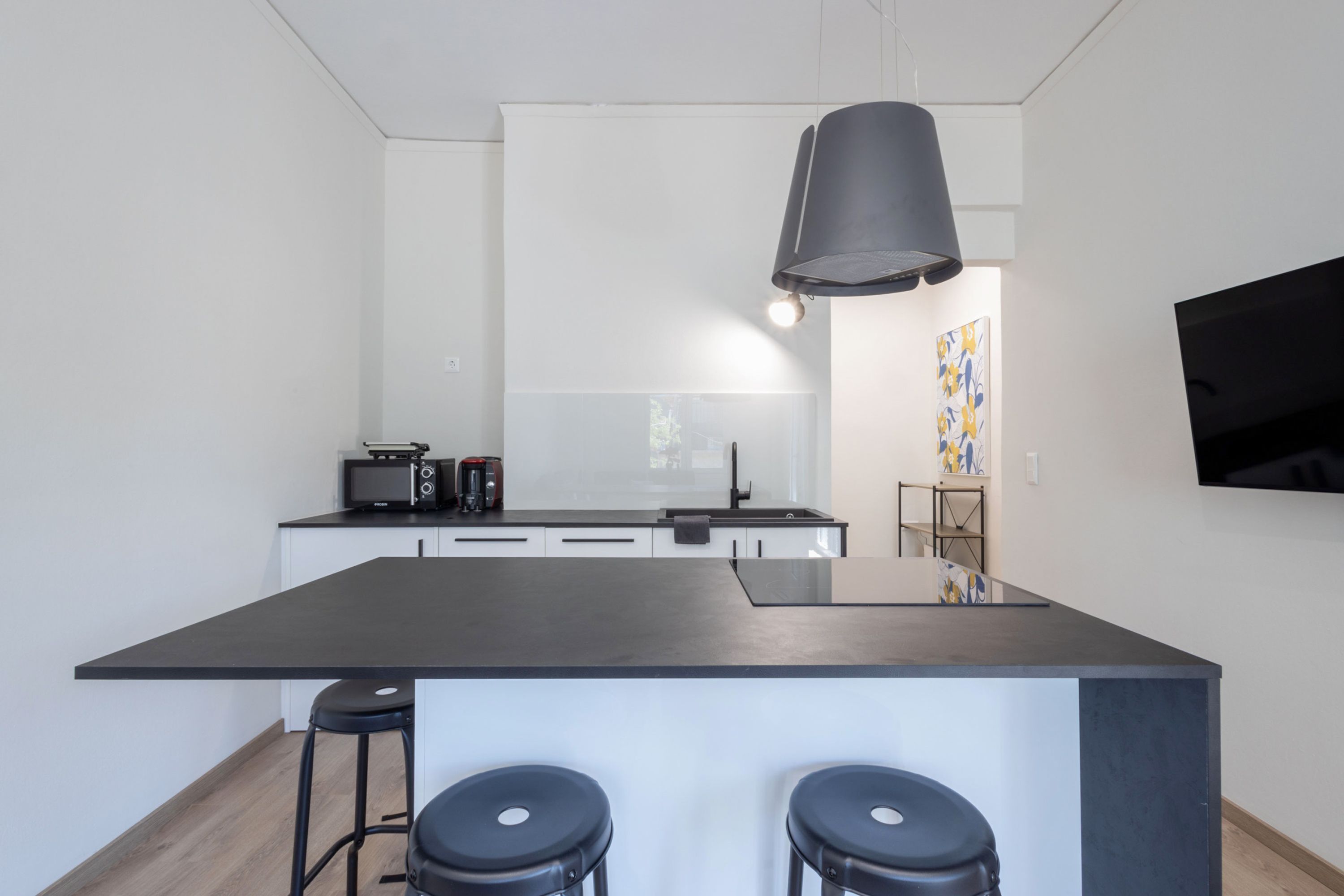 Una cucina moderna con isola centrale, sgabelli da bar, forno a microonde e lampada a sospensione.