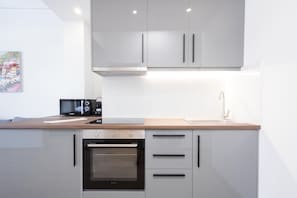 A modern kitchen with white cabinets, a built-in oven, a microwave, and a wooden countertop.
