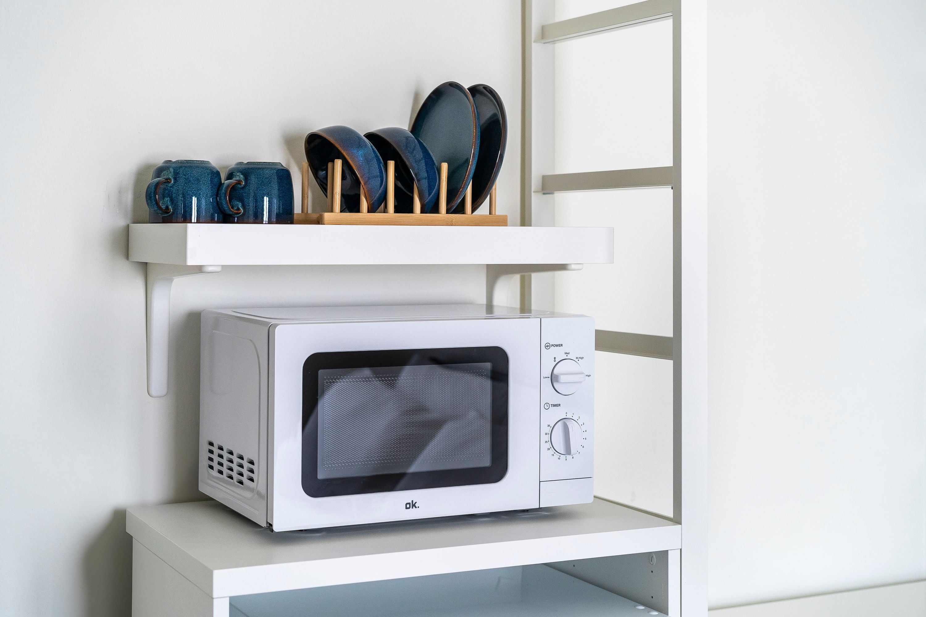 Un four à micro-ondes est posé sur une étagère blanche, au-dessus d’un meuble blanc.