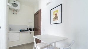 Eine kleine Küchenzeile mit einem weißen Tisch und einer Bank, einem gerahmten Bild an der Wand und einer Tür.