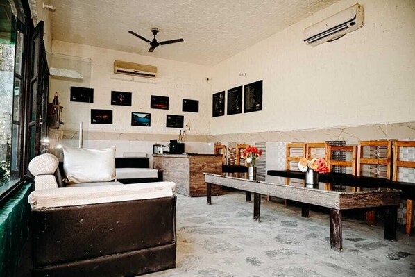 A room with a sofa, a wooden bench, a small table with flowers, and a ceiling fan. - Corbett Tiger Unit of Gadabout Hotels (Kaladhungi)