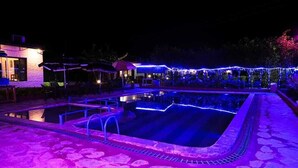 A swimming pool with a stone deck, surrounded by a covered area with umbrellas. - Corbett Tiger Unit of Gadabout Hotels (Kaladhungi)