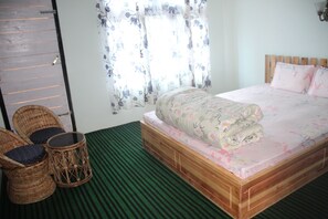 A room with a bed, two wicker chairs, a small round table, and a window with floral curtains.