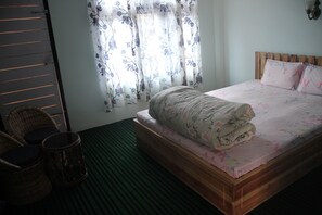 A bedroom with a wooden bed, floral bedding, a window with floral curtains, and a green-striped floor.