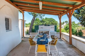 An outdoor patio with a table set for dining, surrounded by chairs, and a barbecue grill in the background. - Trullo del Bosco In Martina Franca (Martina Franca)
