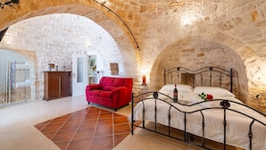 Una habitación con paredes de piedra, una cama, un sillón rojo y un armario de madera.