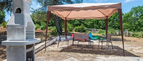 An outdoor patio with a stone grill, a covered seating area, and a playground.