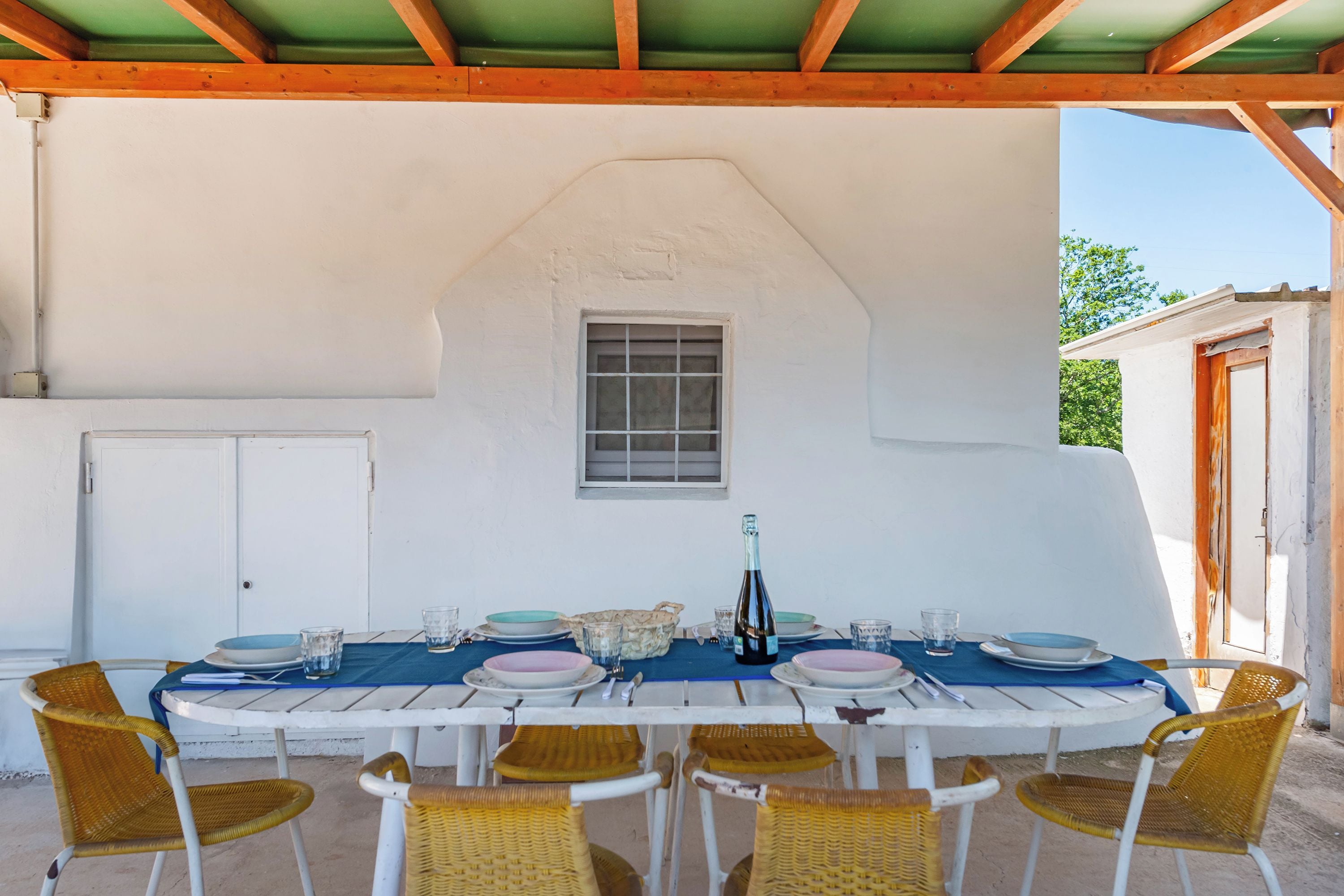 A covered outdoor dining area with a white table set for six, surrounded by wicker chairs.