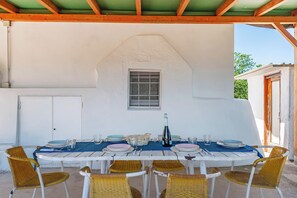 A covered outdoor dining area with a white table set for six, surrounded by wicker chairs. - Trullo del Bosco In Martina Franca (Martina Franca)