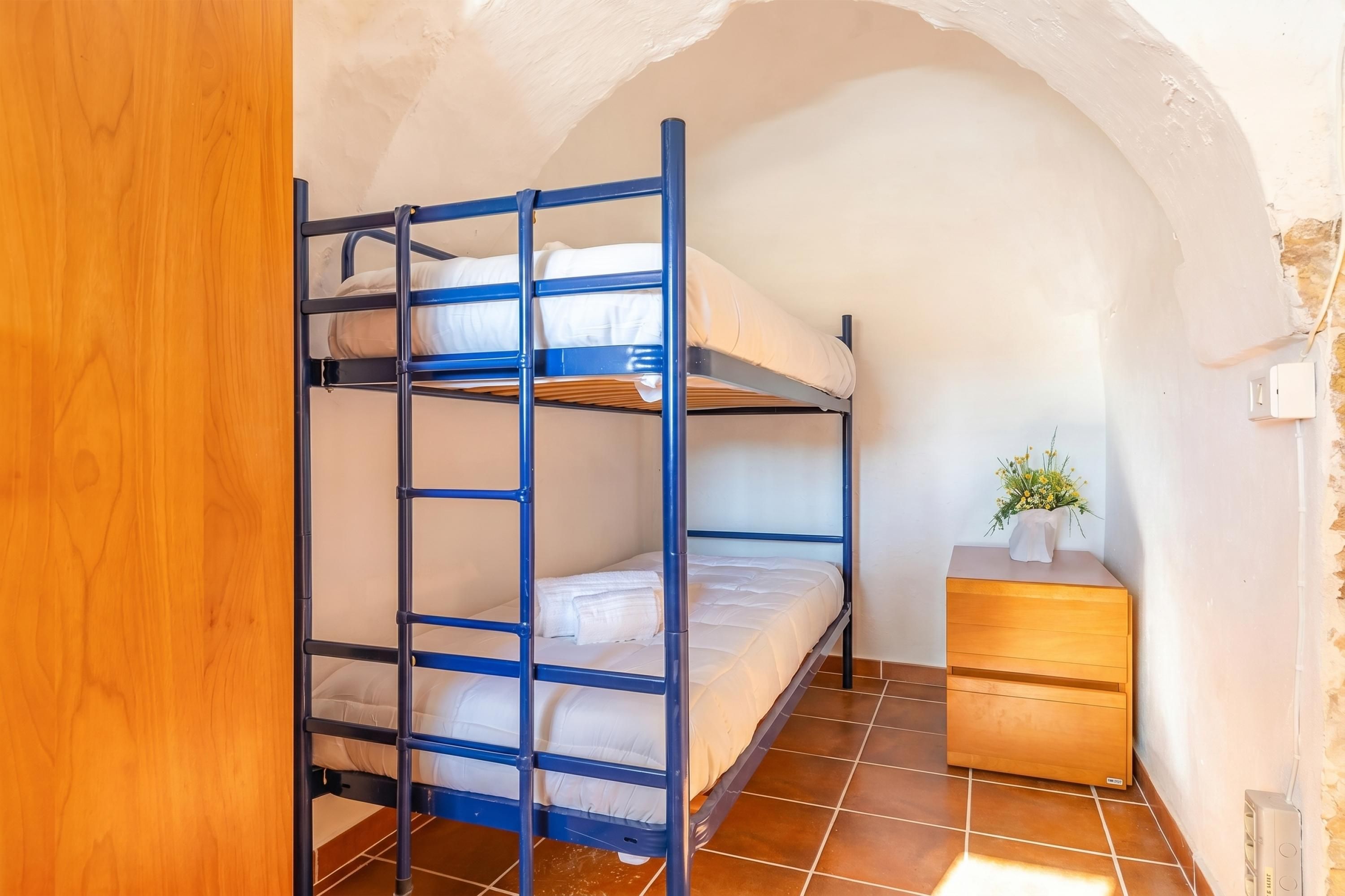 Un letto a castello con una cassettiera in legno e una piccola pianta, in una stanza con soffitto a volta.