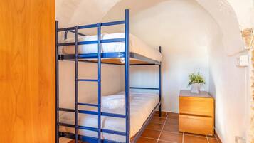 Un letto a castello con una cassettiera in legno e una piccola pianta, in una stanza con soffitto a volta.