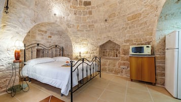 Une chambre aux murs de pierre, avec un lit, une table de chevet, une lampe et un four à micro-ondes posé sur un meuble en bois.