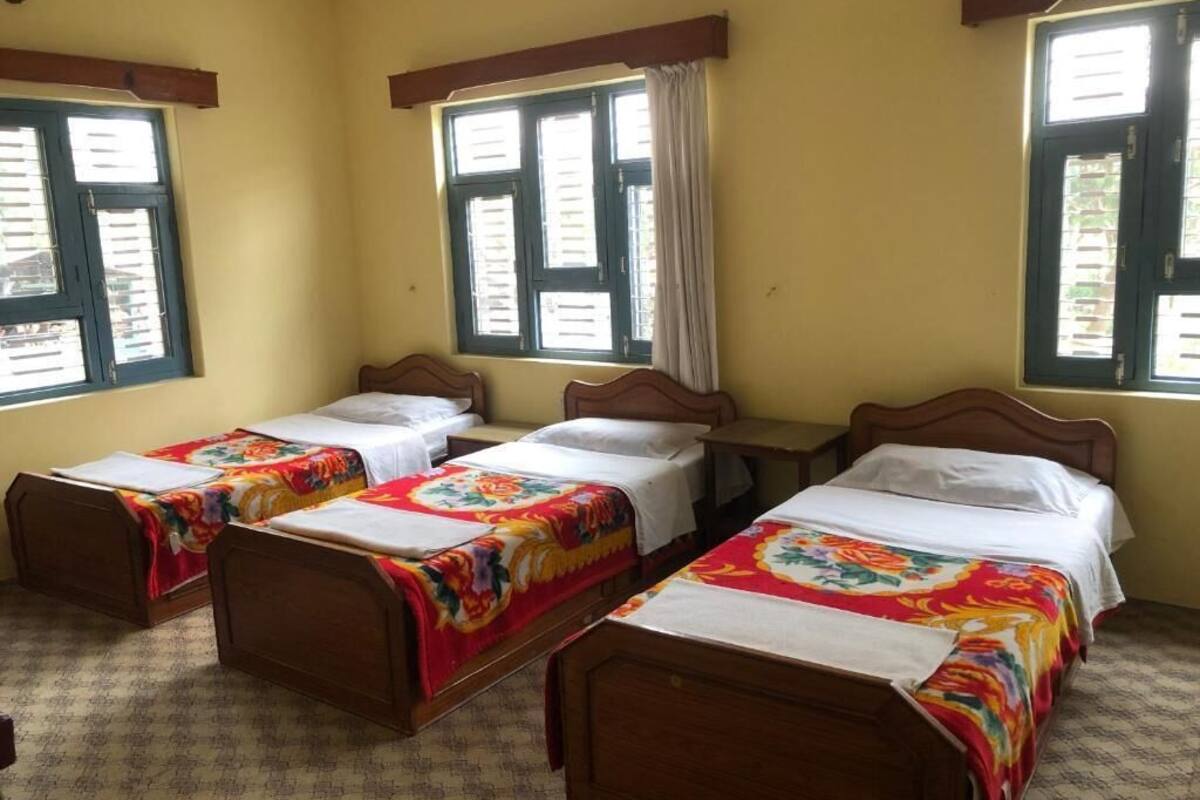 A room with three wooden beds, each with a colorful bedspread. There are windows with curtains, and the walls are painted yellow.
