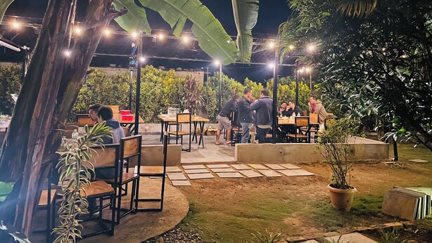 An outdoor dining area with tables and chairs, surrounded by greenery and illuminated by string lights. - Hotel Vibe (Pokhara)
