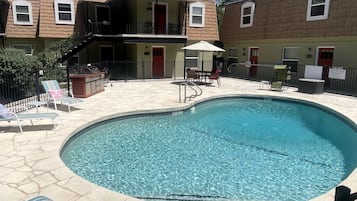 A swimming pool with lounge chairs and a covered seating area, surrounded by a fenced patio.