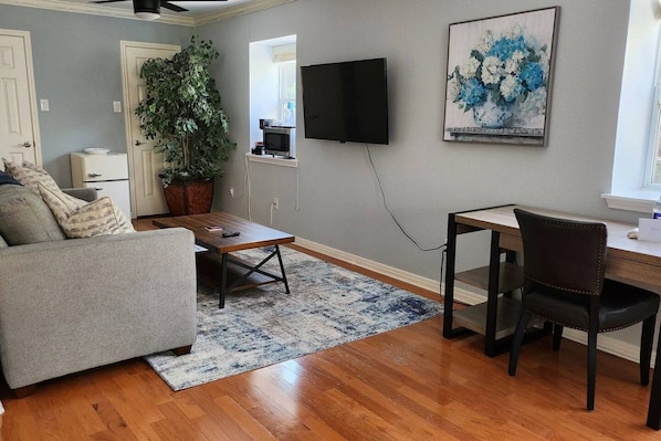 A living room with a sofa, coffee table, TV, and a desk with a chair.