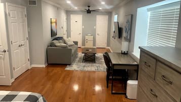 A well-lit room with a ceiling fan, a sofa, a dining table, and a TV mounted on the wall.
