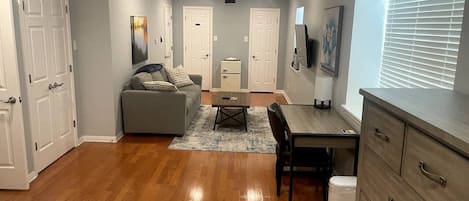 A well-lit room with a ceiling fan, a sofa, a dining table, and a TV mounted on the wall.