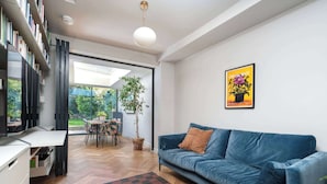 A modern living room with a blue sofa, a dining table, and a bookshelf.