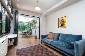 A modern living room with a blue sofa, a dining table, and a bookshelf.