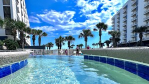 A swimming pool with clear blue water, surrounded by palm trees and modern buildings.