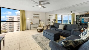 A spacious living room with a large window, a ceiling fan, and a view of the ocean.