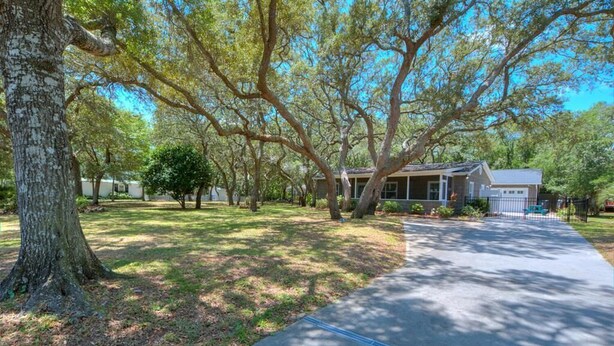 A residential property with a paved driveway, large trees, and a house with a porch. - Heavily Salted: Beach Walk, Game Room, Dog Friendly, Home Gym (Oak Island)