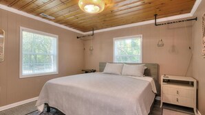 Quarto com cama, duas janelas, ventilador de teto e mesa de cabeceira.