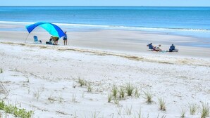 A beach scene with a blue canopy, a chair, and a person standing. - Heavily Salted: Beach Walk, Game Room, Dog Friendly, Home Gym (Oak Island)