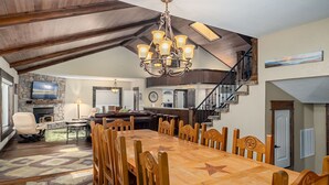 Een ruime eethoek met een lange houten tafel en stoelen, een stenen openhaard en een kroonluchter.