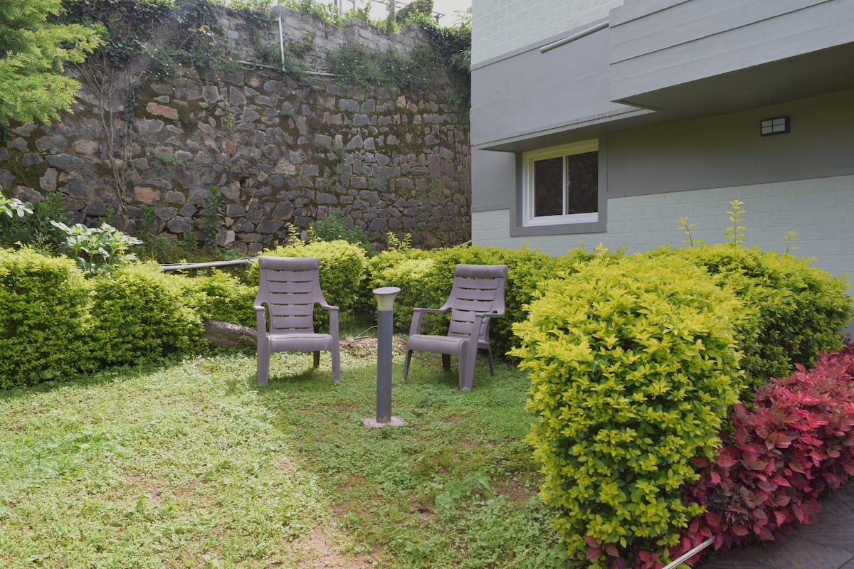Una zona patio con due sedie e un tavolo, circondata da siepi curate e un muro in pietra.