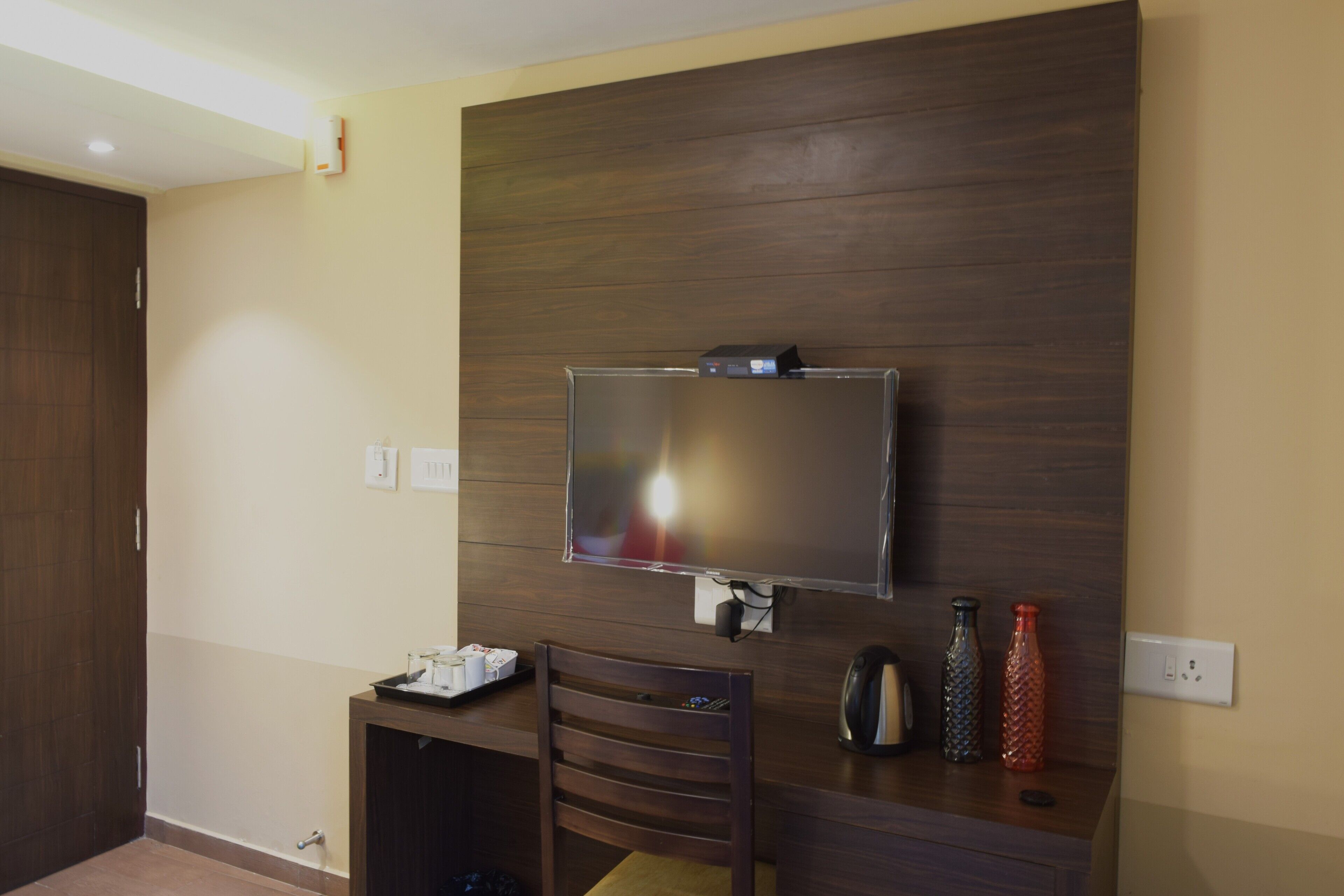 Quarto moderno com televisão de tela plana presa a uma parede de madeira, uma pequena mesa com cadeira e duas garrafas decorativas sobre a mesa.