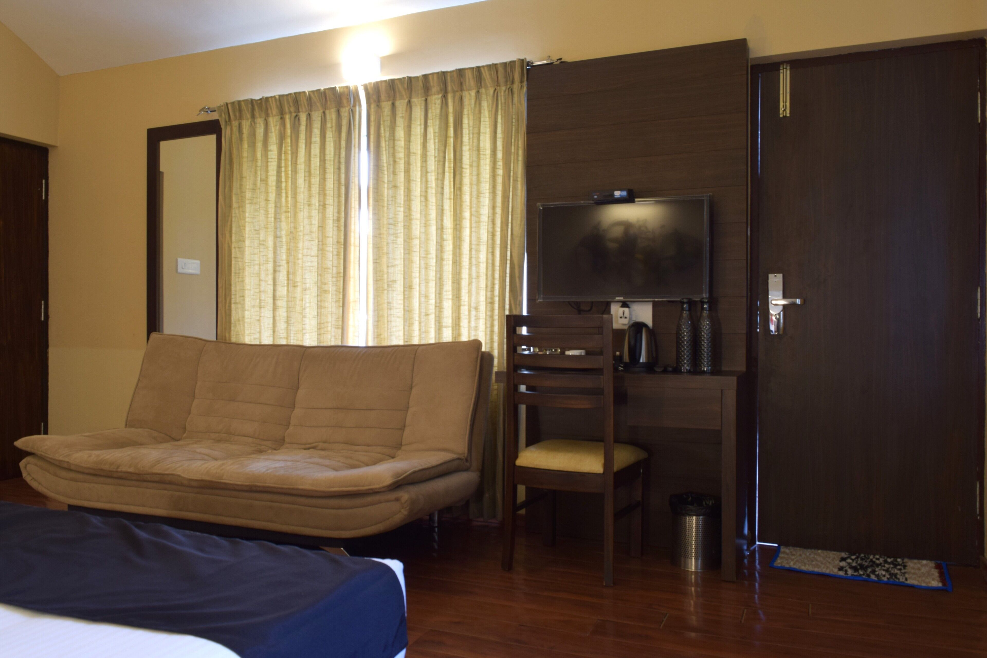 A hotel room with a sofa, a chair, a TV, a desk, and a door.