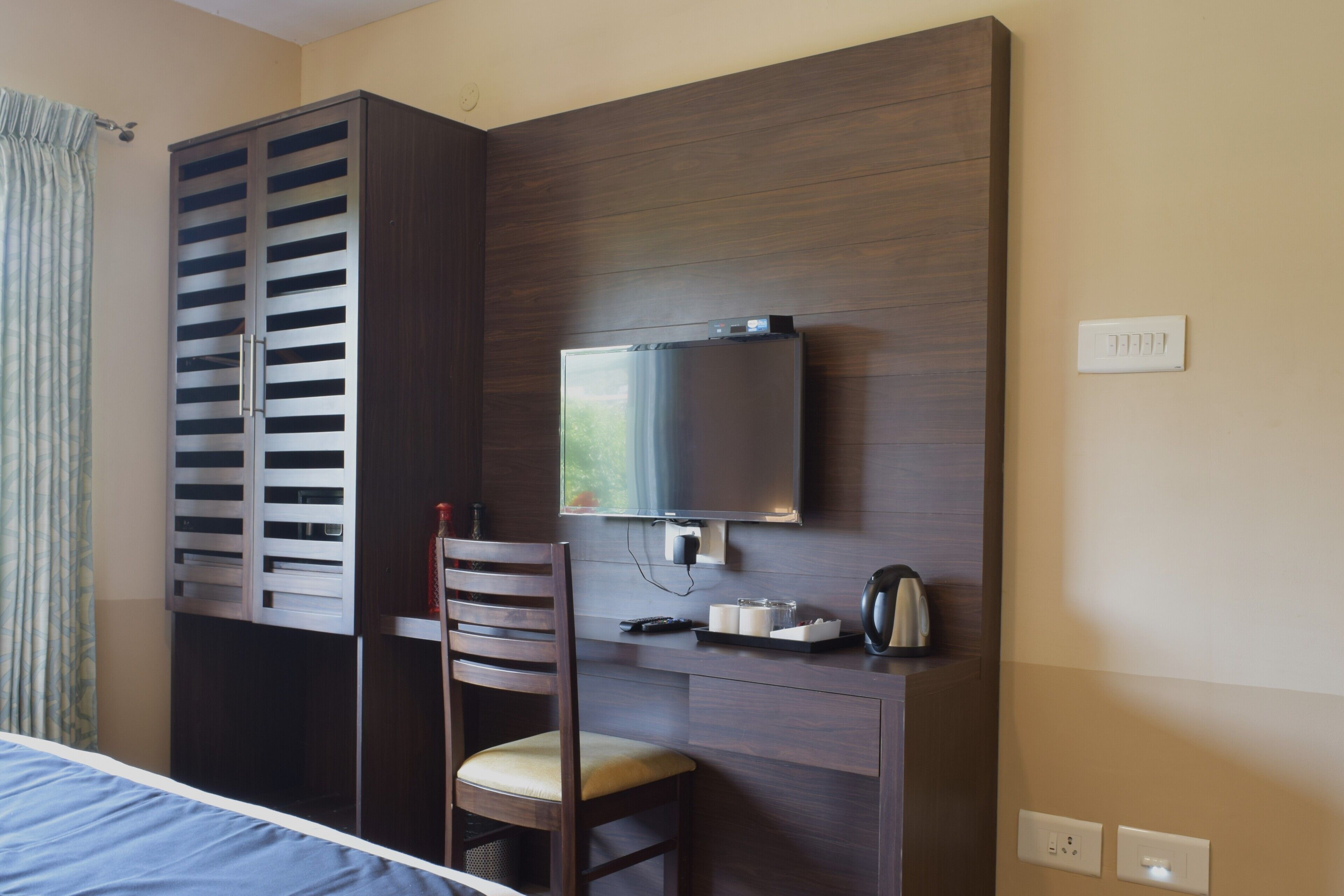 A hotel room with a bed, a wooden desk, a chair, a television, and a wardrobe.