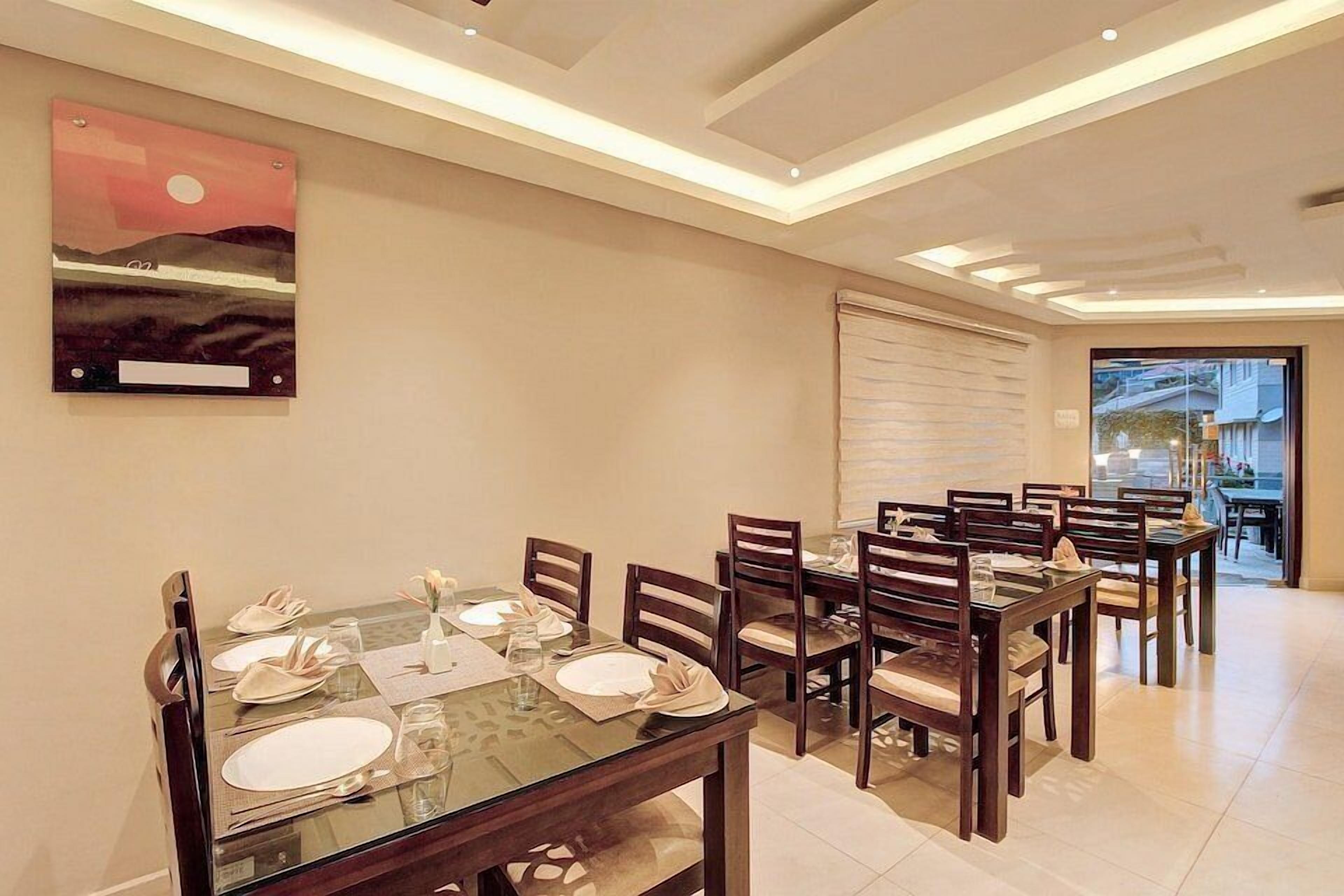 A dining area with a glass table, wooden chairs, and a painting on the wall.