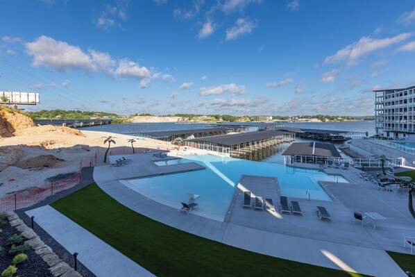 Ein großer Pool mit mehreren Terrassen und Liegebereichen, umgeben von einer bepflanzten Terrasse und Blick auf das Wasser.