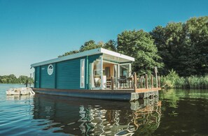 Une péniche flottante dotée d’une terrasse couverte et d’un petit espace salon extérieur.