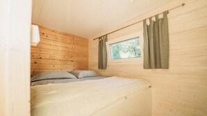 Een gezellige kamer met houten wanden, een bed met een witte dekbedovertrek, twee kussens en een raam met gordijnen.