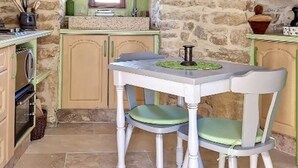 A rustic kitchen with stone walls, a small window, and a table with two chairs.